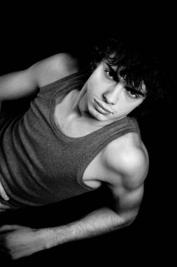 Gri tişörtlü, esmer, genç bir adam beton duvara karşı poz veriyor.