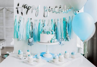 Bir yaşındaki erkek bebeğin onuruna şenlikli bir dekor. Kürsüde beyaz pasta, kekler, mavi toplar ve süslemeler. 