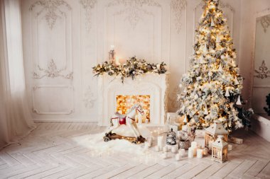 Beyaz bir odanın içinde Noel ağacı, süslü bir şömine, sallanan at ve yeni yıl hediyeleri olan bir oda.