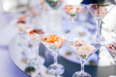 Lüks, zarif bir düğün sofrası. Yanında salata bardakları ve abur cuburlarla servis ediliyor. Ayna yüzeyinde ekmek, mor renkler. Dekorasyon çiçekleri