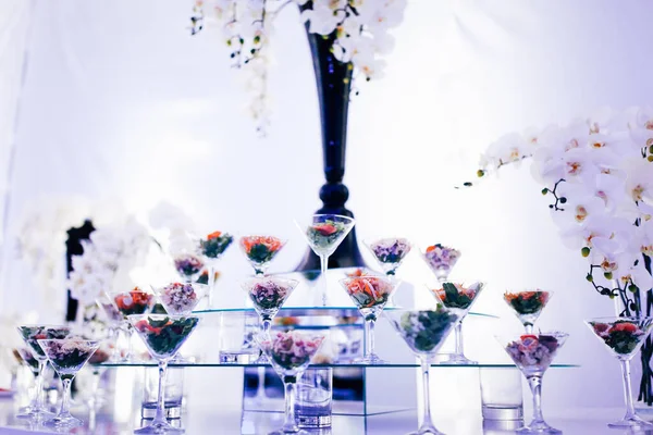 Luxury exquisite wedding catering table served with glasses with salads snacks bread on mirror surfaces purple colors. Decorating flowers