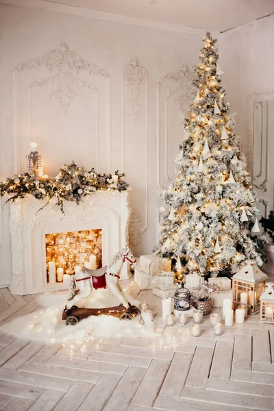 带有花环的圣诞树 装饰过的壁炉 摇曳的马 新年礼物的白色房间的经典内部 — 图库照片