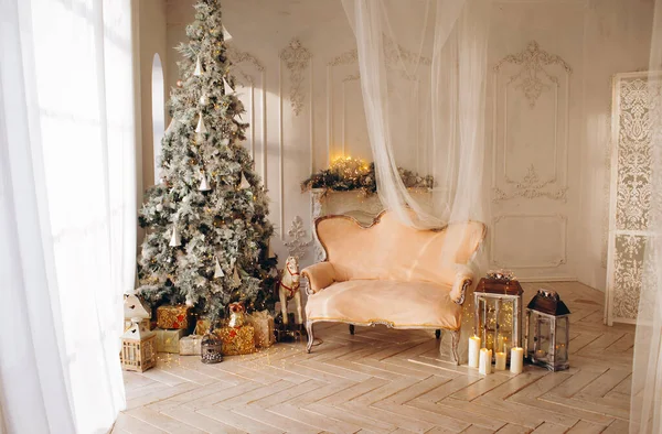 美しいクリスマスの素晴らしい白い古典的なインテリアクリスマスツリー暖炉のソファの装飾のおもちゃの贈り物と大きな窓 — ストック写真