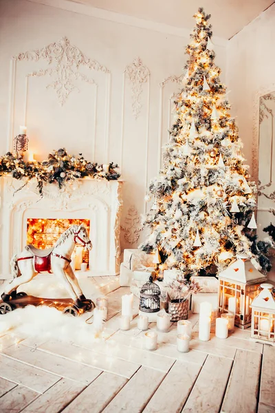 ガーランドとクリスマスツリーと白い部屋の古典的なインテリア 装飾された暖炉 ロッキングホース 新年のための贈り物 — ストック写真