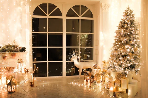 warm and cozy evening in Christmas interior design, Xmas tree decorated by lights presents gifts, toys, deer, candles, lanterns, garland lighting indoors fireplace. holiday living room magic New year
