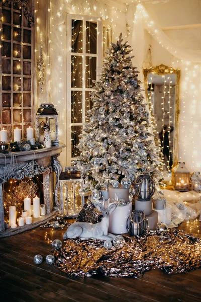 warm and cozy evening in Christmas interior design,Xmas tree decorated by lights presents gifts,toys, deer,candles, lanterns, garland lighting indoors fireplace.holiday living room.magic New year