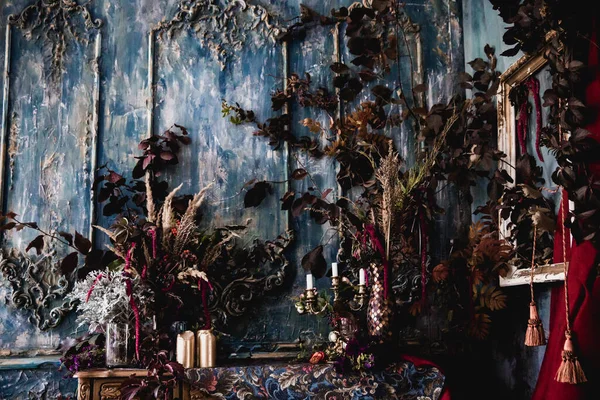 Kurumuş çiçekler, vazolar, avizeler, altın çerçeveli kumaşlar, lüks kraliyet tarzı ahşap bir masa, eski fenerlerle yanan mumlar.