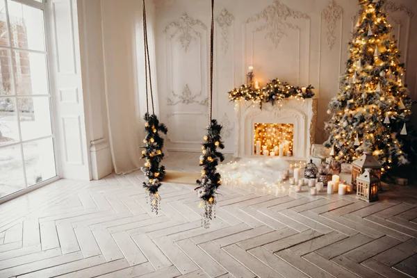 classical interior of decorated white room with swing, decorated fireplace, Christmas tree, garlands, candles,lanterns, gifts on background