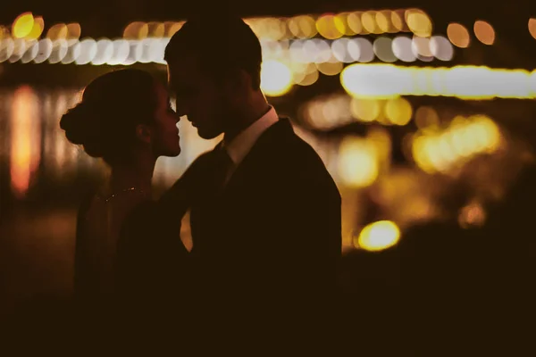 Şık giyinmiş zarif bir çift akşam vakti dışarıda sarılıyor.