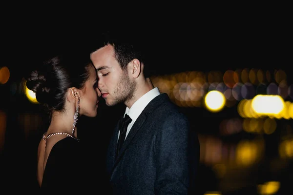 Şık giyinmiş zarif bir çift akşam vakti dışarıda sarılıyor.