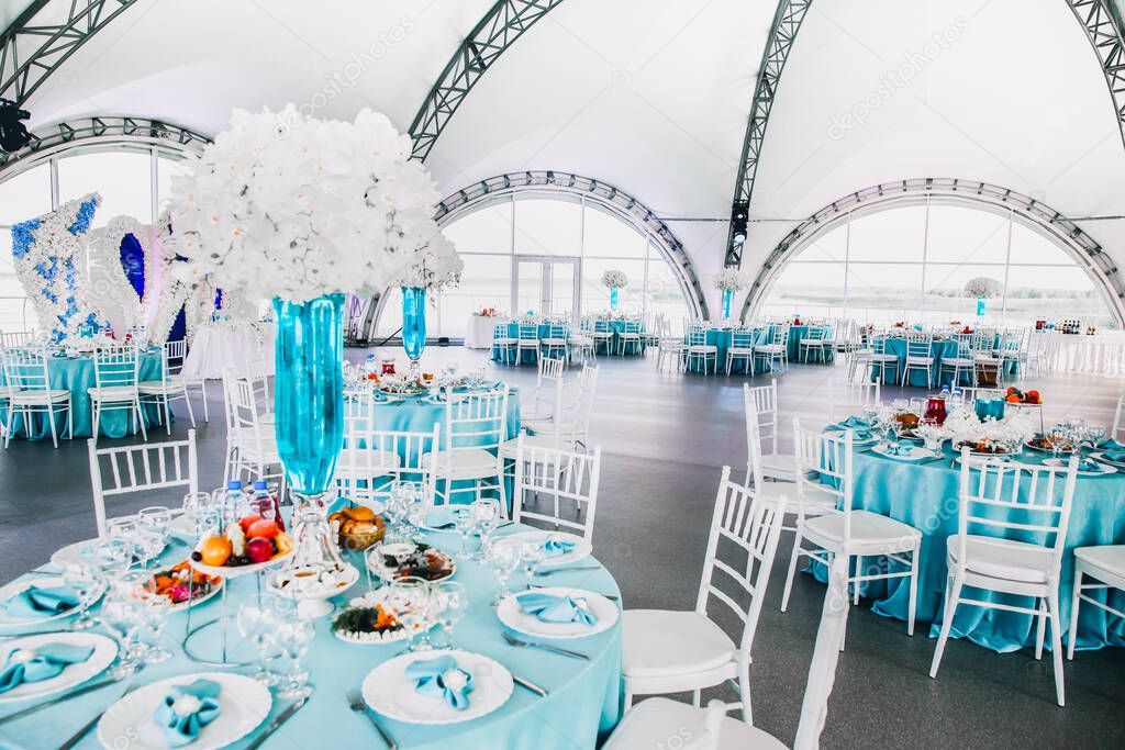 Big beautiful decorated restaurant at the wedding, wedding in blue and white colors, orchids flowers in vases with blue water