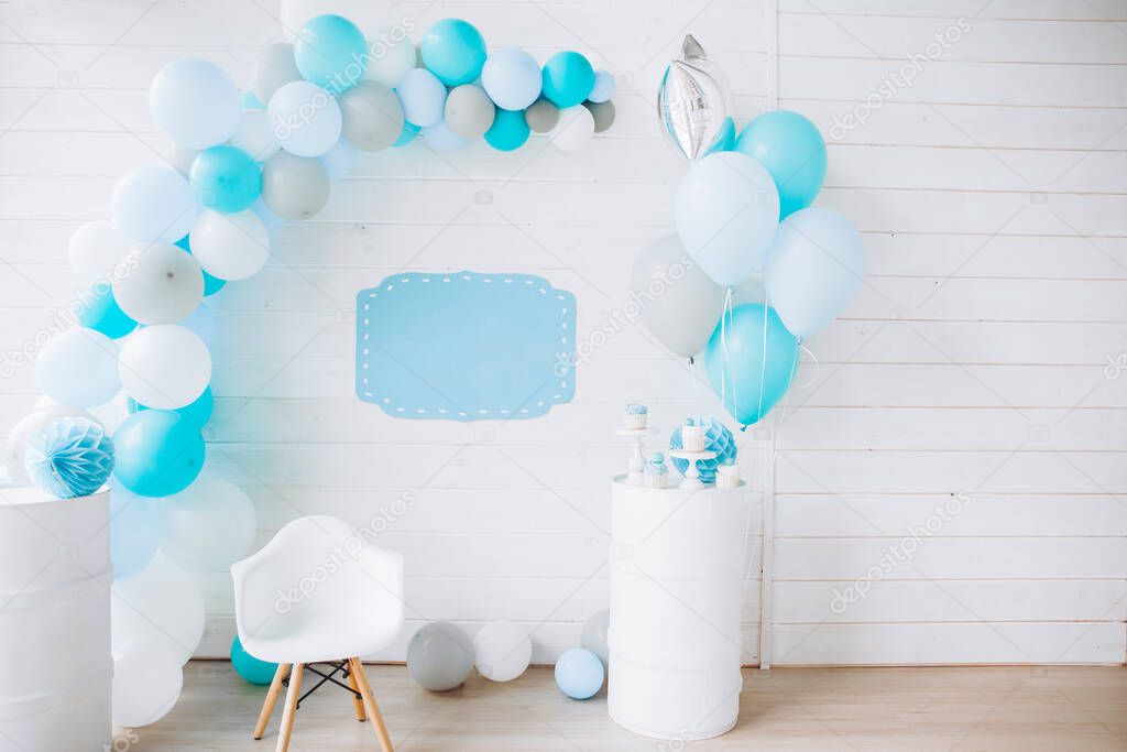 festive white wooden wall decorated with an arch of balloons, blue color, a plate for inscription blank, happy birthday concept