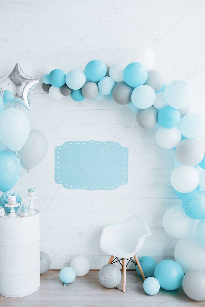 festive white wooden wall decorated with an arch of balloons, blue color, a plate for inscription blank, happy birthday concept