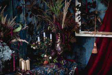 Kurumuş çiçekler, vazolar, avizeler, altın çerçeveli kumaşlar, lüks kraliyet tarzı ahşap bir masa, eski fenerlerle yanan mumlar.