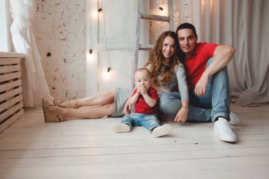 Mutlu ebeveynler, erkek bebekle odada poz veriyorlar.