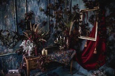 Kurumuş çiçekler, vazolar, avizeler, altın çerçeveli kumaşlar, lüks kraliyet tarzı ahşap bir masa, eski fenerlerle yanan mumlar.