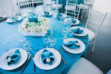 Düğünde mavi ve beyaz renklerde güzel dekore edilmiş restoranlar masa örtüleriyle servis edilen masa örtüleri, tekstil peçeteleri vazolarda mavi suyla servis edilen çiçekler.