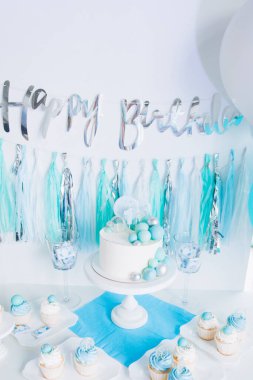 Bir yaşındaki erkek bebeğin onuruna şenlikli bir dekor. Kürsüde beyaz pasta, kekler, mavi toplar ve süslemeler. 