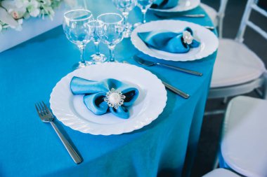 Beyaz çiçekli düğün masası ve kristalli mavi peçeteler.