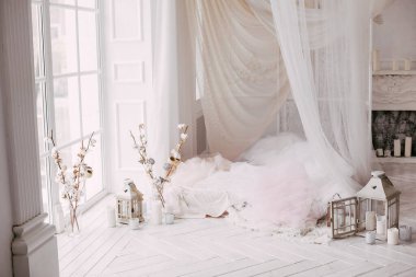 Beyaz ahşap zemin penceresi olan büyük, temiz, parlak bir oda, lale perdeleriyle süslenmiş bir yatak, pamuk dallarla süslenmiş vazolar.