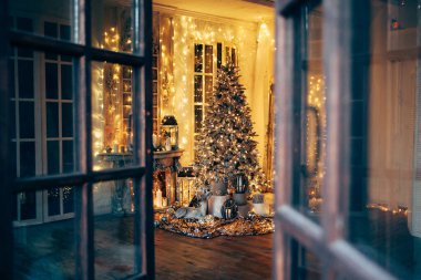 Noel iç tasarımında sıcak ve sıcak bir akşam, ışıklarla süslenmiş Xmas ağacı hediyeler, oyuncaklar, geyikler, mumlar, fenerler, kapalı alanda yanan çelenkler.