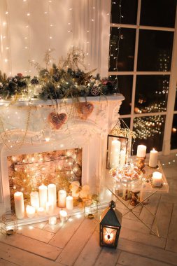 Noel iç tasarımında sıcak ve sıcak bir akşam, ışıklarla süslenmiş Xmas ağacı hediyeler, oyuncaklar, geyikler, mumlar, fenerler, kapalı alanda yanan şömine. tatil salonu sihirli yeni yıl