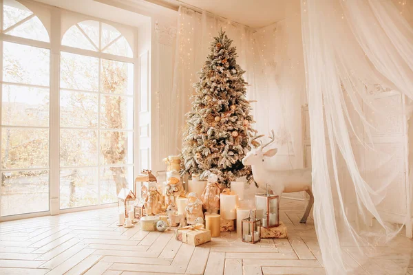 Warm and cozy morning in Christmas interior design, Xmas tree decorated by lights presents, gifts, toys, deer, candles, lanterns, garland lighting, indoors fireplace.