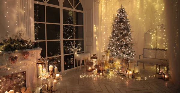 Noel iç tasarımında sıcak ve sıcak bir akşam, ışıklarla süslenmiş Xmas ağacı hediyeler, oyuncaklar, geyikler, mumlar, fenerler, kapalı alanda yanan çelenkler.