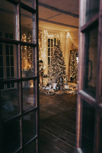 warm and cozy evening in Christmas interior design,Xmas tree decorated by lights presents gifts,toys, deer,candles, lanterns, garland lighting indoors fireplace.holiday living room.magic New year