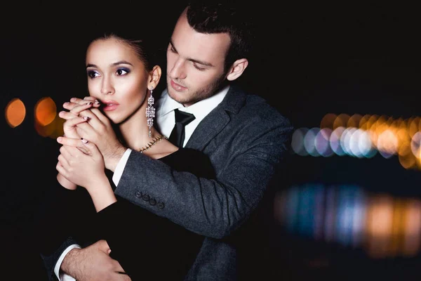 穿着时髦服装的年轻夫妇晚上在外面拥抱 免版税图库照片