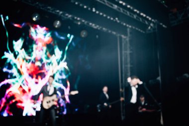 Parlak spot ışıklarının kırmızı mavi ışıklarıyla sahnede şarkı söyleyen şarkıcı ve rock grubunun bulanık renkli fotoğrafı