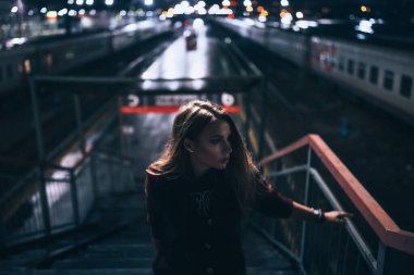 Güzel, genç, yalnız bir kız merdivenlerde dikiliyor. Tren istasyonunun arkasında ışıklar sokak gecelerindeki su birikintilerine yansıyor, yağmur yağıyor, trenin yan tarafa bakmasını bekliyor.