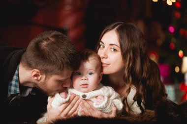 Mutlu ebeveynler oğullarıyla birlikte ayı halısına, şömineye ve arka plandaki ışıklara uzanırlar.