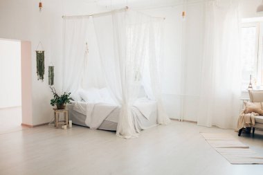 Minimalist İskandinav tarzı bir yatak odasında rahat bir yatak odası, örtülü yatak, battaniye yastıkları, bitki. Günaydın güneşli fotoğraf.