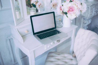 Çiçek, sandalye ve dekorlu beyaz tuvalet masasında gümüş dizüstü bilgisayar