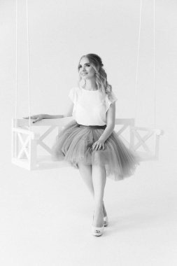 Şık etekli ve bluzlu güzel sarışın manken ahşap salıncakta oturuyor.