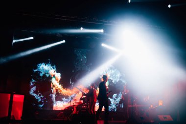 Parlak spot ışıklarının kırmızı mavi ışıklarıyla sahnede şarkı söyleyen şarkıcı ve rock grubunun bulanık renkli fotoğrafı