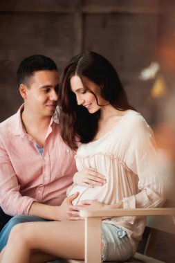 Güzel bir çift bankta oturuyor, hamile bir kadın ve kocası tahta bir arka planda.