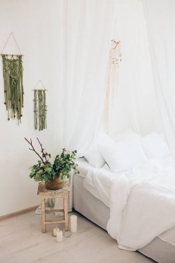 Minimalist İskandinav tarzı bir yatak odasında rahat bir yatak odası, örtülü yatak, battaniye yastıkları, bitki. Günaydın güneşli fotoğraf.
