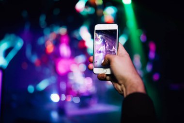 Konserdeki hayran elinde bir akıllı telefon tutuyor ve fotoğraf çekiyor ya da arka planda video çekiyor. Bir şarkıcı ve müzik grubunun bulanık performansı.