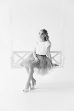 Şık etekli ve bluzlu güzel sarışın manken ahşap salıncakta oturuyor.