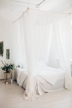 Minimalist İskandinav tarzı bir yatak odasında rahat bir yatak odası, örtülü yatak, battaniye yastıkları, bitki. Günaydın güneşli fotoğraf.