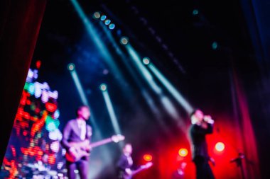 Parlak spot ışıklarının kırmızı mavi ışıklarıyla sahnede şarkı söyleyen şarkıcı ve rock grubunun bulanık renkli fotoğrafı