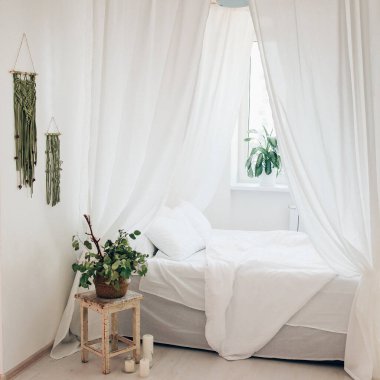 Minimalist İskandinav tarzı bir yatak odasında rahat bir yatak odası, örtülü yatak, battaniye yastıkları, bitki. Günaydın güneşli fotoğraf.