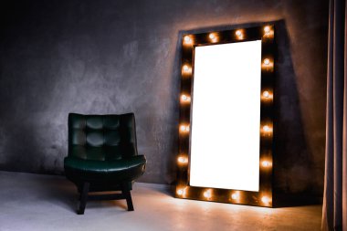 yeşil deri koltuk ve uzun giyinme aynası. Koyu renkli bir odada, gri bir duvarın arka planında, üzerinde lambalar olan bir çerçeve.