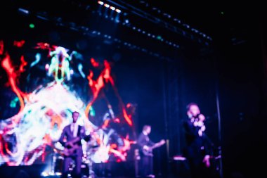 Parlak spot ışıklarının kırmızı mavi ışıklarıyla sahnede şarkı söyleyen şarkıcı ve rock grubunun bulanık renkli fotoğrafı