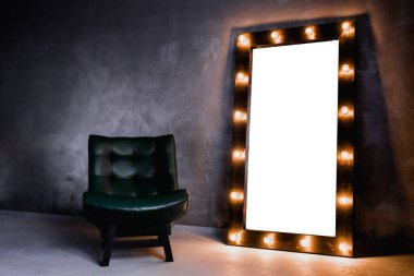 yeşil deri koltuk ve uzun giyinme aynası. Koyu renkli bir odada, gri bir duvarın arka planında, üzerinde lambalar olan bir çerçeve.