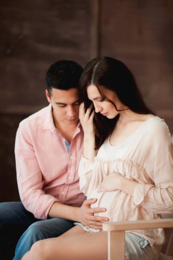 Güzel bir çift bankta oturuyor, hamile bir kadın ve kocası tahta bir arka planda.