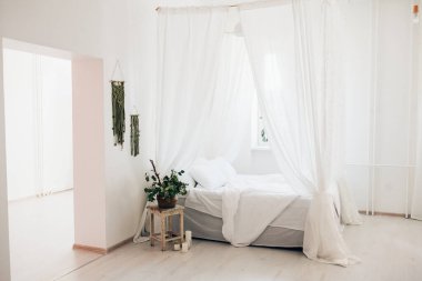 Minimalist İskandinav tarzı bir yatak odasında rahat bir yatak odası, örtülü yatak, battaniye yastıkları, bitki. Günaydın güneşli fotoğraf.