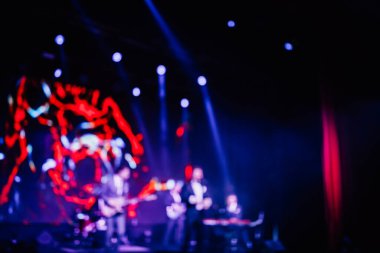 Parlak spot ışıklarının kırmızı mavi ışıklarıyla sahnede şarkı söyleyen şarkıcı ve rock grubunun bulanık renkli fotoğrafı